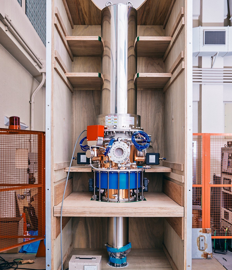 Gyrotron, a large silver pipe placed vertically is connected to a golden pipe in the middle, and round instruments and blue cords and more are attached at the connection.