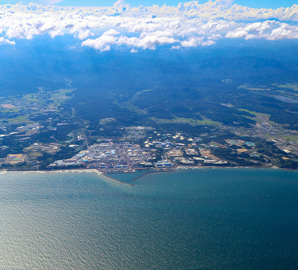 A distant view of the Fukushima Daiichi Nuclear Power Station, captured from the sea, with the mountains and clouds on the background