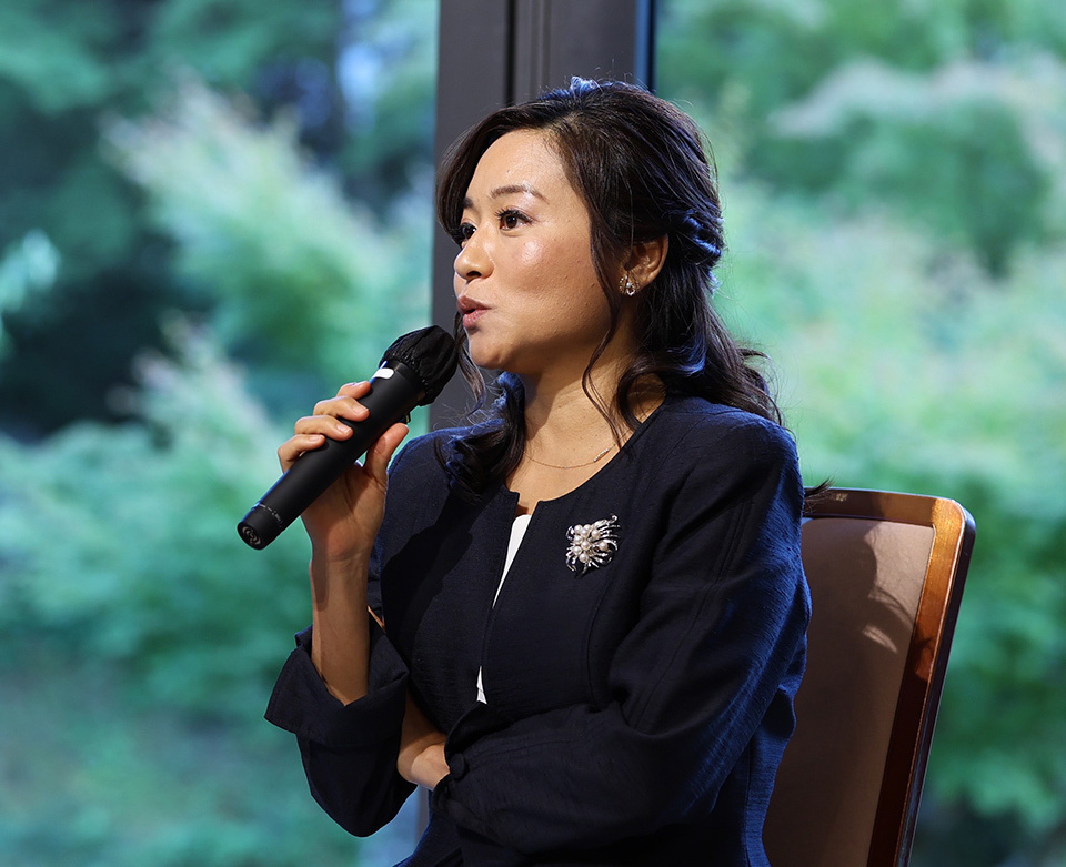 Emi Onozuka, CEO of Eminent Group, speaking at a conference with a green backdrop.