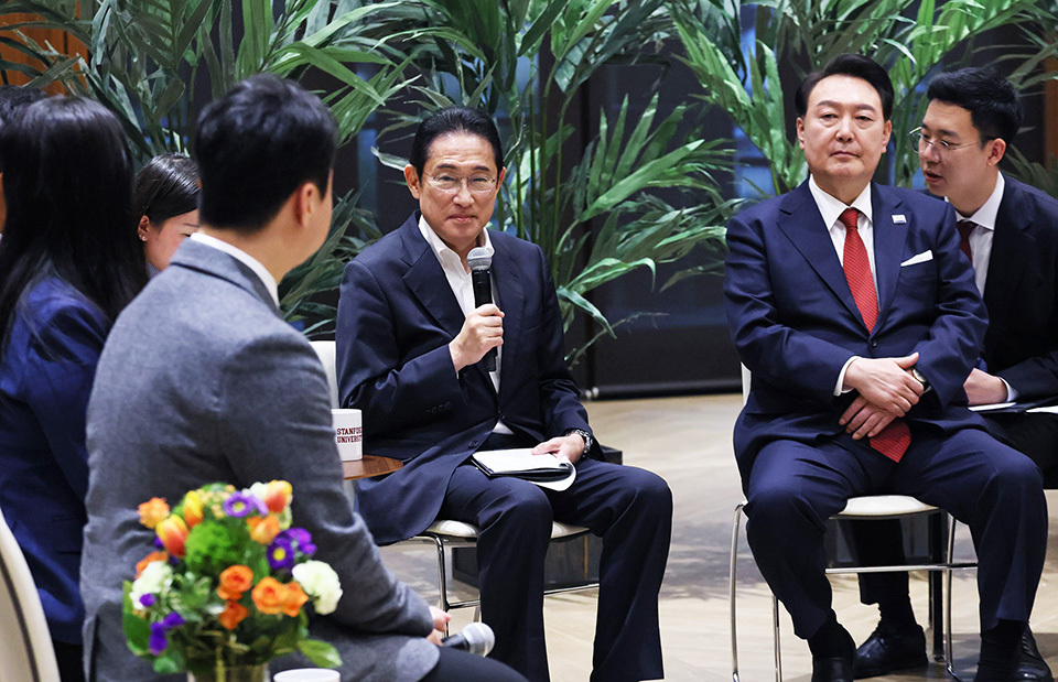 A group of individuals, including the leaders of Japan and Korea, are seated in a semi-circle with well-maintained potted plants in the background.