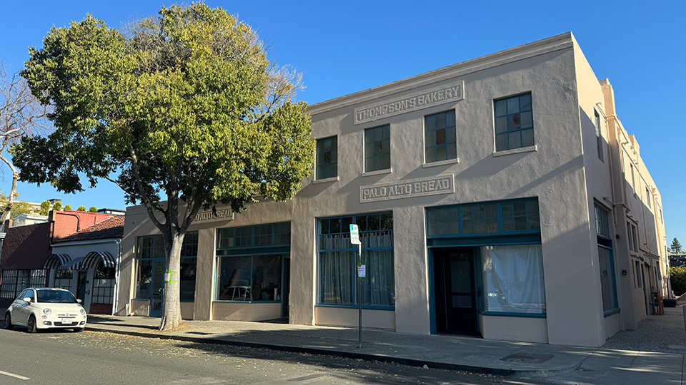 A two-story brown building with large rectangular windows, situated on a sunny street corner.