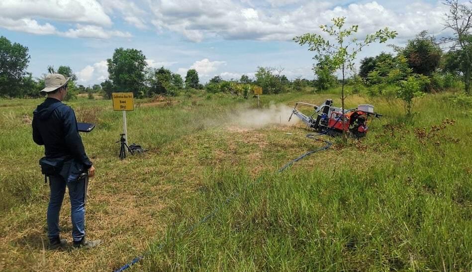 A man remotely operates a machine in a minefield, using compressed air to clear soil for mine excavation.