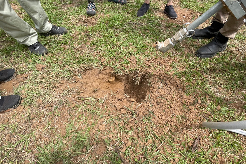 Several people standing together, closely examining a hole in the ground at an outdoor location.