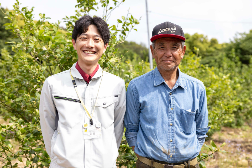 Two men smiling and standing in front of a lemon grove