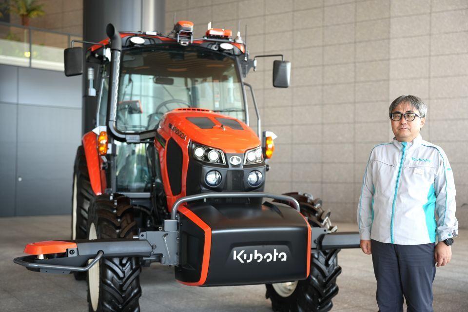 Man in a grey and blue jacket posing by a Kubota combine harvester