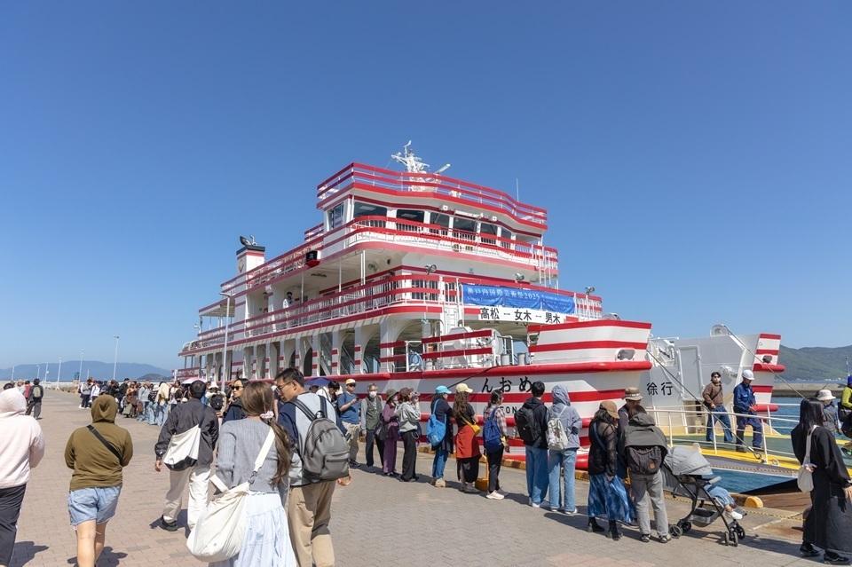 Visitors from various countries looking at a red and white striped boat. 