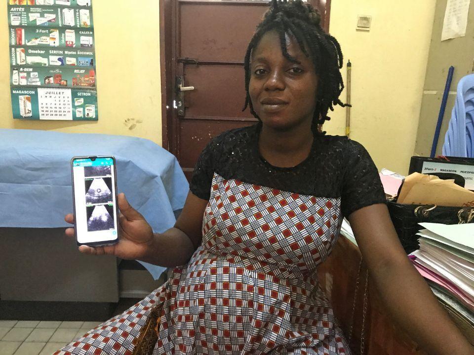 A pregrant woman with short braids showing a sonogram on a smartphone