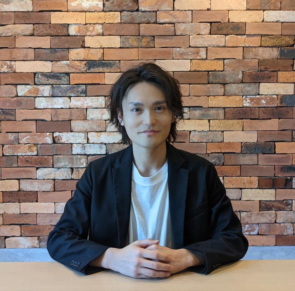 Watanabe Yusuke, the SEO of Reev Inc., sitting in front of a brick wall